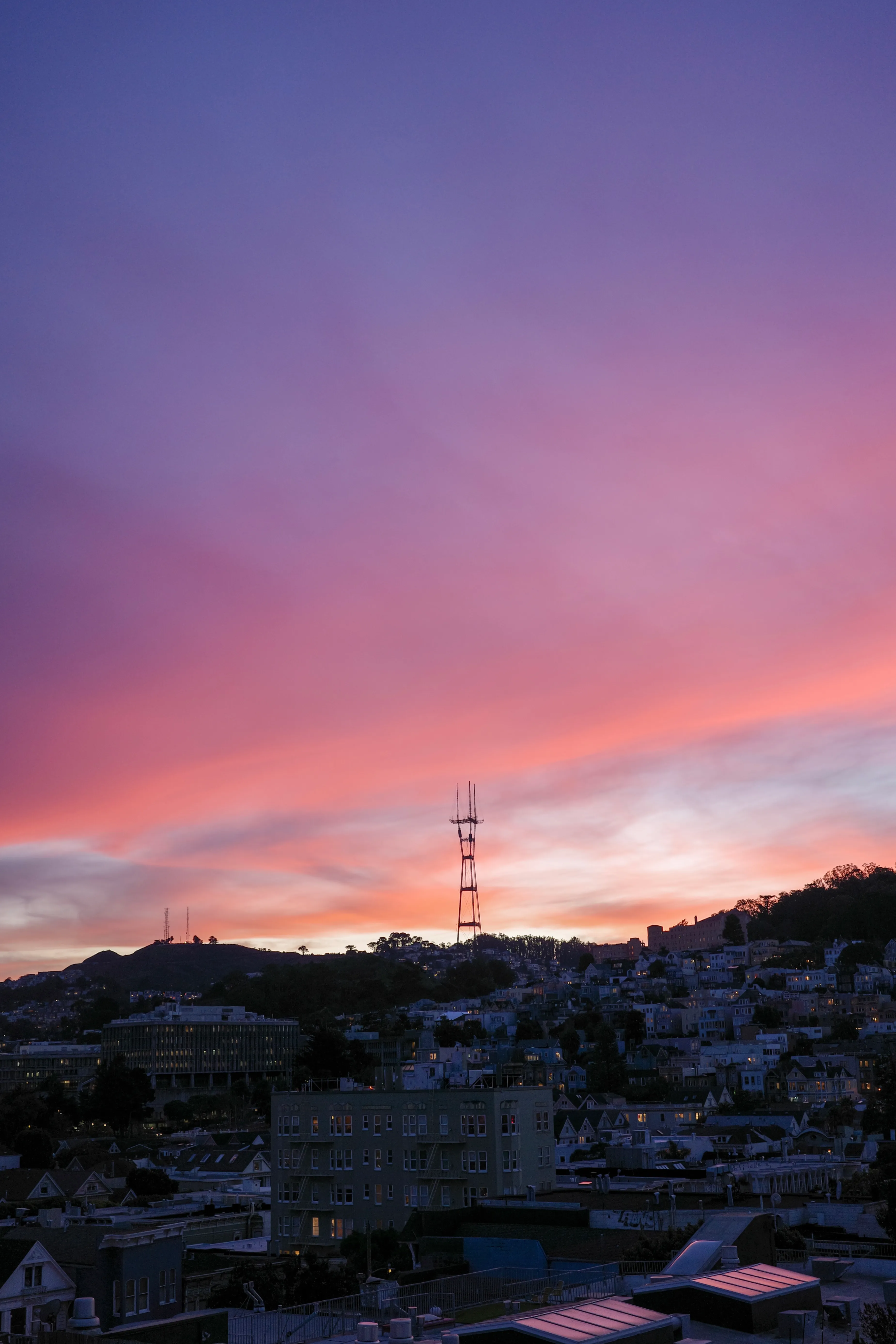 Pink and violet sunset clouds over San Francisco rooftops, with Sutro Tower silhouetted on the hill